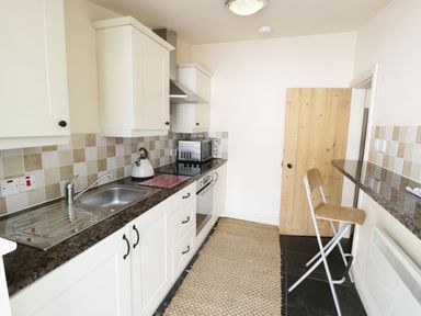 A kitchen with a sink stove microwave and a wooden chair at Menai Cottage in Brynsiencyn