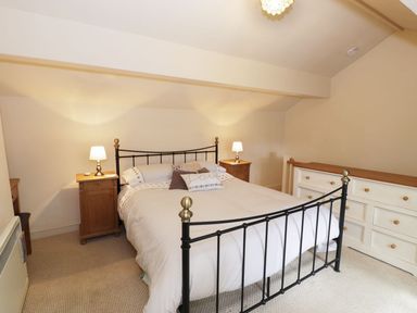 A bedroom with a black metal bed frame bedside tables with lamps and a white dresser at Menai Cottage in Brynsiencyn