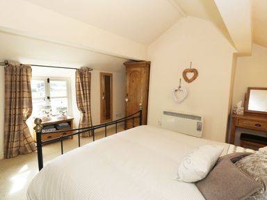 A bedroom with a bed a wooden wardrobe a window with curtains and a dresser at Menai Cottage in Brynsiencyn
