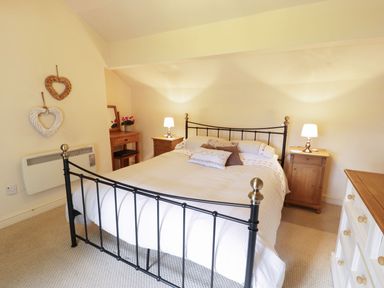 A bedroom with a black metal bed frame two wooden bedside tables with lamps a wooden dressing table with a mirror and flowers heart decorations on the wall at Menai Cottage in Brynsiencyn