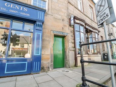 A street view showing a green door labeled Pringles Yard between a blue shopfront and a stone building with large windows at 1 Pringles Yard in Alnwick