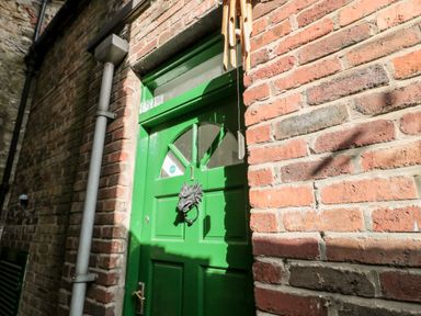 A green door with a dragon-shaped knocker set in a brick wall at 1 Pringles Yard in Alnwick