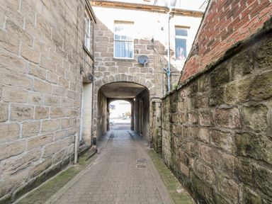 A narrow alley with stone and brick walls leading to an arched passage at 1 Pringles Yard in Alnwick