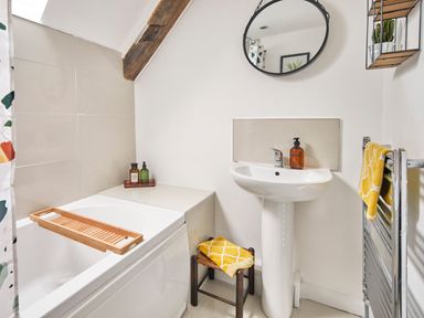 A bathroom with a bathtub a sink a round wall mirror and a towel on a stool at 1 Pringles Yard in Alnwick