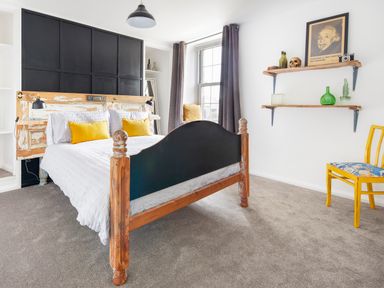 A bedroom with a wooden bed frame white bedding yellow pillows wooden shelves with decorations and a yellow chair at 1 Pringles Yard in Alnwick