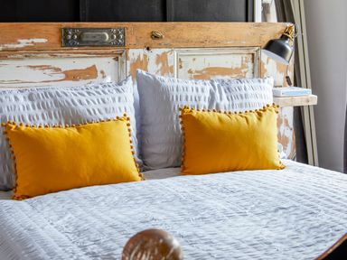 A bed with white bedding and two yellow pillows with a rustic wooden headboard at 1 Pringles Yard in Alnwick