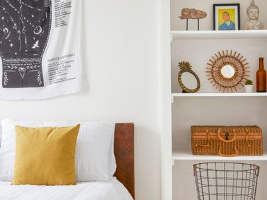 A bedroom with a white bed and yellow pillow next to white shelves with decorations and a wicker basket at 1 Pringles Yard in Alnwick