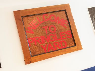 A wooden framed sign with red text reading Welcome to Pringles Yard on a white wall at 1 Pringles Yard in Alnwick