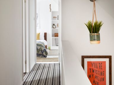 A hallway with striped carpet leading to a bedroom with a bed and shelves at 1 Pringles Yard in Alnwick