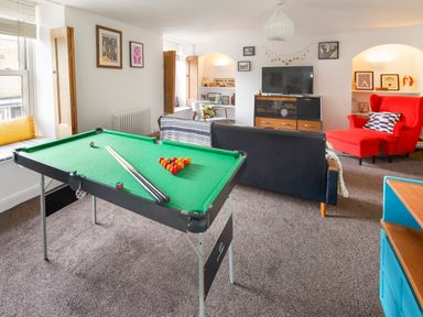 A living room with a pool table a black sofa a red armchair and a television at 1 Pringles Yard in Alnwick
