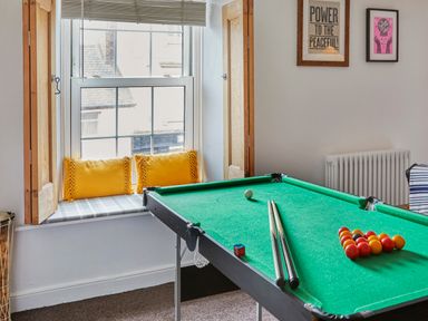 A room with a pool table next to a window with yellow cushions and framed pictures on a wall at 1 Pringles Yard in Alnwick
