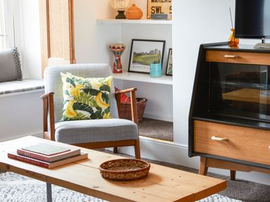 A living room with a wooden chair with a banana patterned cushion a wooden coffee table with books and a wicker basket shelves with decor and a wooden TV stand at 1 Pringles Yard in Alnwick