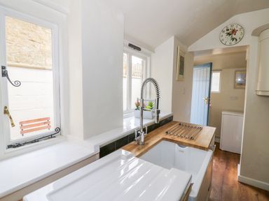 A kitchen with a sink and faucet next to windows and a wooden countertop at Victoria Cottage in Chipping Norton