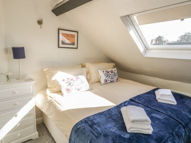 A bedroom with a bed a bedside table with a lamp a framed picture on the wall and a skylight window at Victoria Cottage in Chipping Norton