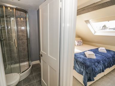 A bathroom with a curved glass shower enclosure and a bedroom with a bed and a skylight window at Victoria Cottage in Chipping Norton