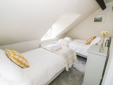 A bedroom with two single beds with checkered pillows and blankets a window and a dresser with flowers at Victoria Cottage in Chipping Norton