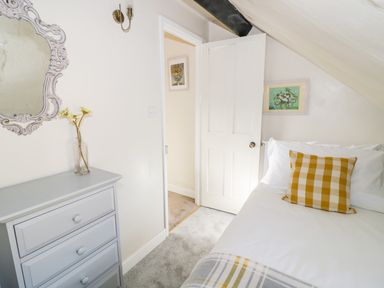 A bedroom with a gray chest of drawers a bed with a checkered pillow and an open door at Victoria Cottage in Chipping Norton