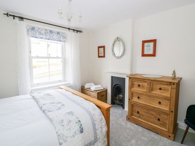 A bedroom with a wooden bed chest of drawers and a small fireplace at Victoria Cottage in Chipping Norton