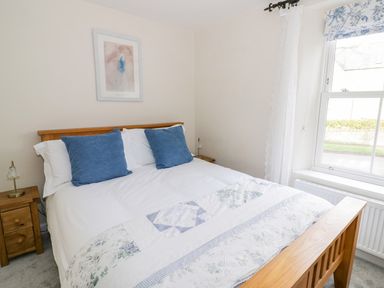 A bedroom with a wooden bed with blue cushions and white bedding at Victoria Cottage in Chipping Norton