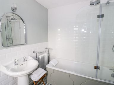 A bathroom with a sink a mirror a bathtub with a showerhead and towels at Victoria Cottage in Chipping Norton