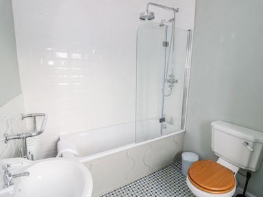 A bathroom with a bathtub shower combination a sink and a toilet with a wooden seat at Victoria Cottage in Chipping Norton