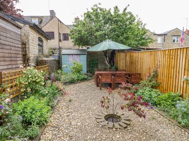 A garden with gravel pathway wooden fence wooden table with umbrella and chairs and a blue shed at Victoria Cottage in Chipping Norton