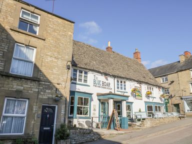 Exterior of a pub and dining room named The Blue Boar with benches and hanging flower baskets in Chipping Norton