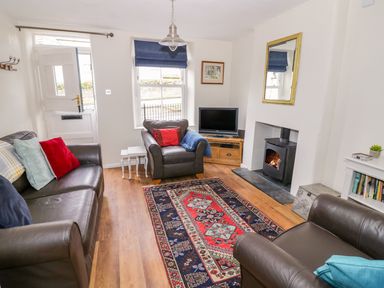 A sitting room with leather sofas a patterned rug a wood burning stove and a television at Victoria Cottage in Chipping Norton