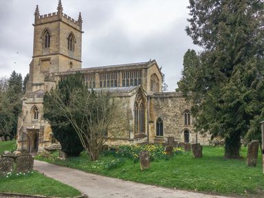 An old stone church with a tower surrounded by trees and gravestones in a grassy area