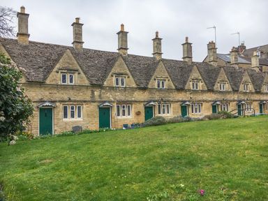 A row of stone cottages with green doors and small windows in front of a grassy lawn at Victoria Cottage in Chipping Norton