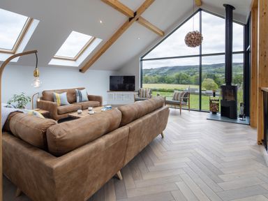 A living room with leather sofas a wood stove and large windows overlooking a green landscape at Gatesgarth in Coniston