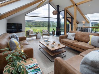 A living room with brown sofas a coffee table two armchairs a television and large windows overlooking fields at Gatesgarth in Coniston