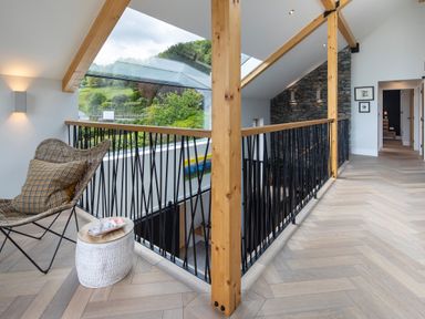 A hallway with wooden beams and a chair near a railing overlooking a lower floor at Gatesgarth in Coniston