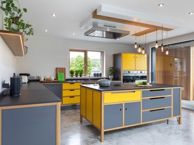 A kitchen with yellow and gray cabinets an island with a pot hanging light bulbs and plants on a shelf and windowsill at Gatesgarth in Coniston