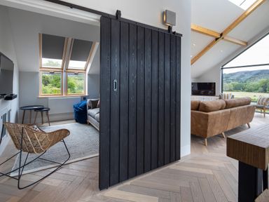 A living room with a brown sofa and a television and a smaller room with a wicker chair and sofa separated by a black sliding door at Gatesgarth in Coniston