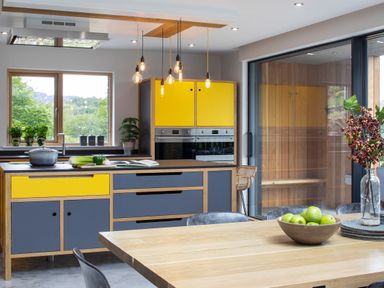 A kitchen with yellow and gray cabinets a wooden dining table with a bowl of green apples and a glass vase with berries at Gatesgarth in Coniston