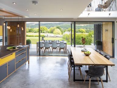 A kitchen and dining area with wooden tables and black chairs overlooking a green landscape at Gatesgarth in Coniston