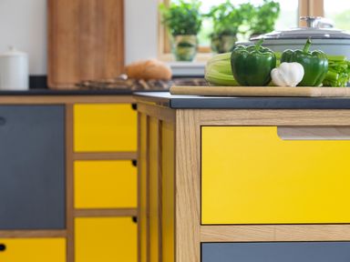 A kitchen with yellow and gray cabinets a cutting board with green peppers garlic and celery on a countertop