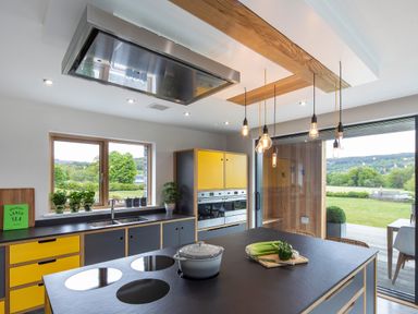 A kitchen with yellow and black cabinets a black countertop with a pot and vegetables a window and sliding glass door showing a green outdoor area at Gatesgarth Coniston