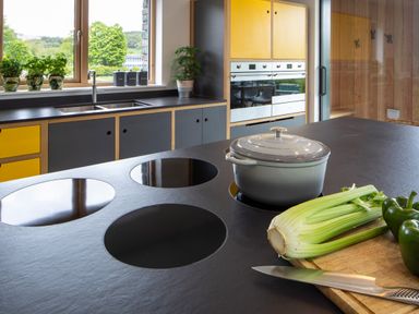 A kitchen with a black countertop island stove a knife celery green peppers a pot sink window and cabinets at Gatesgarth in Coniston