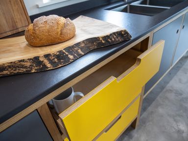 A kitchen countertop with a wooden cutting board and round loaf of bread over yellow drawers at Gatesgarth in Coniston