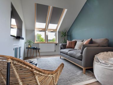 A living room with a gray sofa, a rattan chair, skylight windows, a small side table with a plant, and a wall-mounted television at Gatesgarth in Coniston