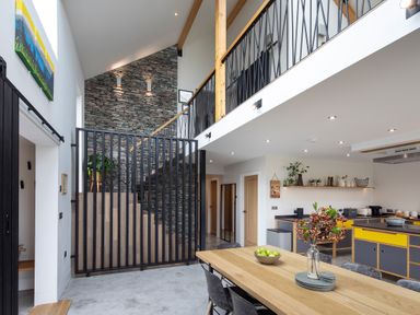 A dining area with a wooden table and chairs next to an open kitchen and a staircase with a stone wall at Gatesgarth in Coniston
