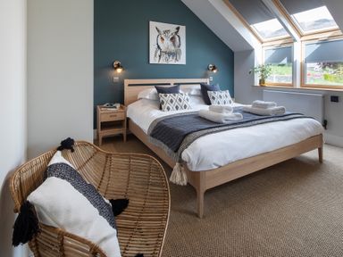 A bedroom with a bed and pillows next to windows and a wicker chair with a cushion at Gatesgarth in Coniston