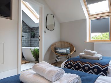 A bedroom with two beds folded towels on each bed a chair with a pillow and an ensuite bathroom with a bathtub and skylight at Gatesgarth in Coniston