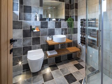 A bathroom with black and gray tiles a white toilet a round sink on a wooden counter and a glass shower at Gatesgarth in Coniston