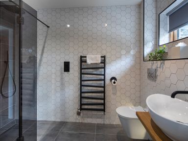 A bathroom with a walk-in shower a black towel rack a white toilet a vessel sink and hexagonal wall tiles at Gatesgarth in Coniston