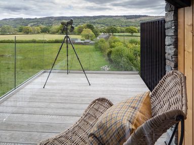 A balcony with a wicker chair and pillow and a tripod with binoculars overlooking a green field at Gatesgarth in Coniston