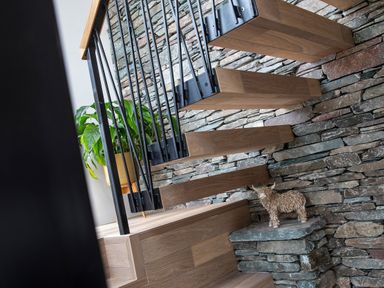 A staircase with wooden steps black metal railing a stone wall a potted plant and a small animal sculpture at Gatesgarth in Coniston