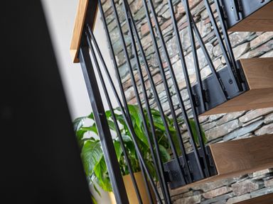 A wooden staircase with black metal railing and a green plant in a yellow pot against a stone wall at Gatesgarth in Coniston